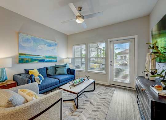 a living room with a blue couch and a ceiling fan at Century Mundy Mill Apartments, Oakwood 30566