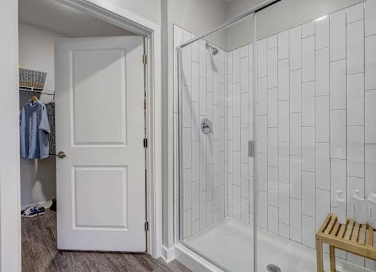 a shower with a glass door in a white tiled bathroom at Century Mundy Mill Apartments, Oakwood, GA 30566