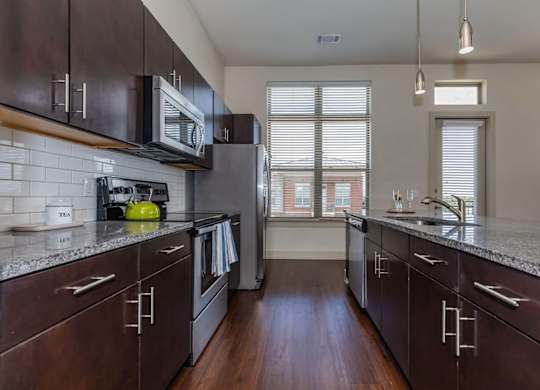 A kitchen with dark wood cabinets and a granite countertop.at Century Cedar Hill, Cedar Hill, 75104