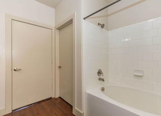 A white tiled bathroom with a bathtub and a door.at Century Cedar Hill, Texas
