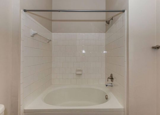 A white tiled bathroom with a white bathtub and a white toilet.at Century Cedar Hill, Cedar Hill, TX 75104