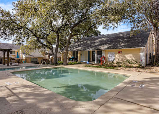A pool surrounded by trees and a building in the background.