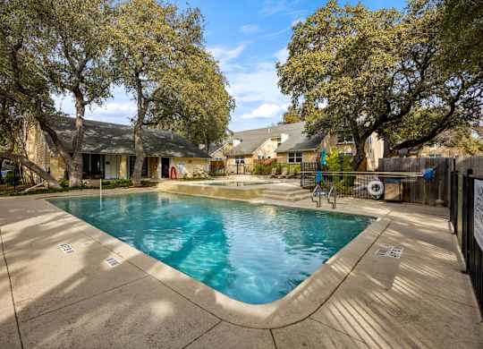 A small pool surrounded by a concrete patio and trees.