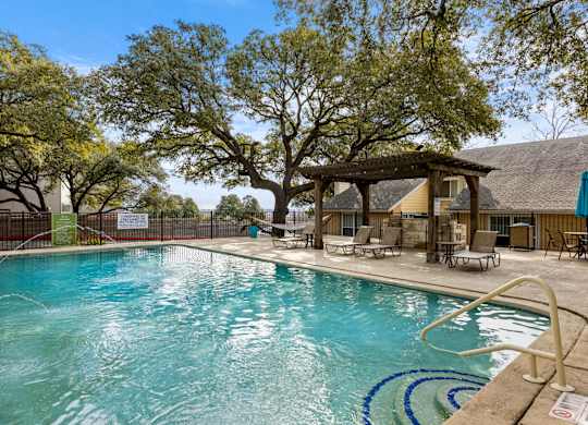 A large swimming pool surrounded by trees and lounge chairs.