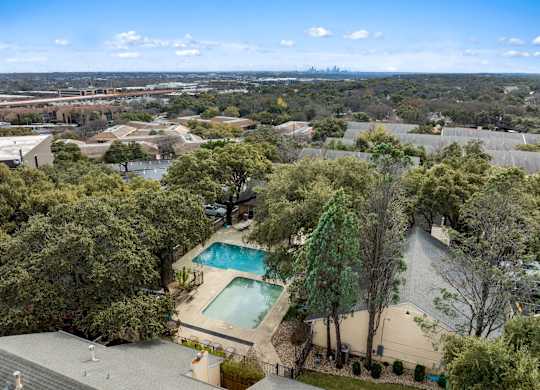 A bird's eye view of a house with a swimming pool surrounded by trees.
