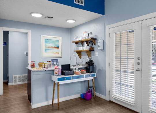 A kitchen area with a table and a shelf with various items on it.