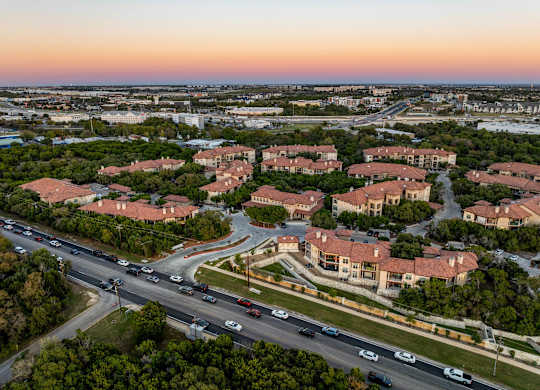 A sunset view of a highway with cars driving and apartment buildings on the side. at Bridge at Heritage Woods, Texas, 78753