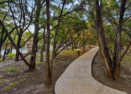 A concrete walkway leads through a grove of trees. at Bridge at Heritage Woods, Texas