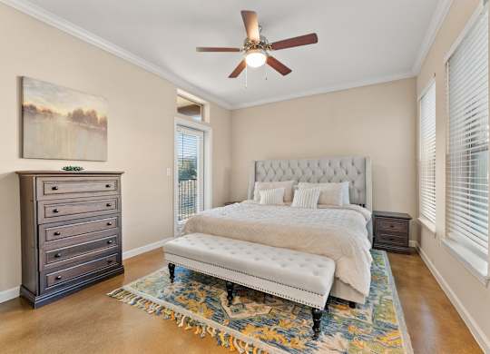 A bedroom with a large bed, a dresser, and a ceiling fan. at Bridge at Heritage Woods, Austin, Texas