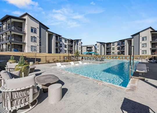 A swimming pool surrounded by lounge chairs and concrete planters in front of apartment buildings. at Bridge at Tech Crossing, Austin, 78753