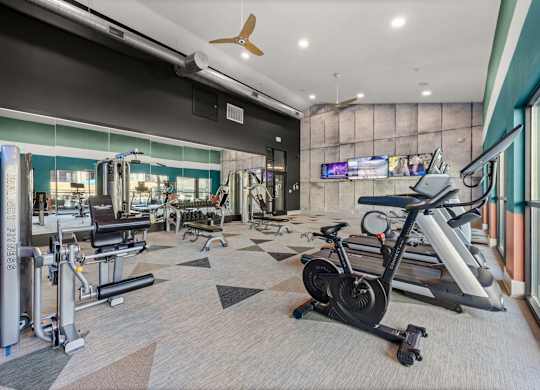 A gym with a variety of equipment including treadmills, weights, and a television. at Bridge at Tech Crossing, Austin, 78753