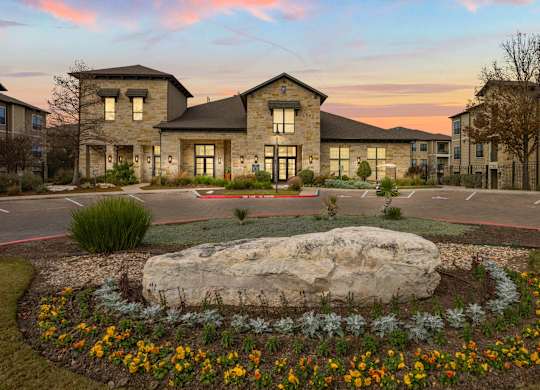 A large rock is in the middle of a flower bed in front of a building. at The Royce at 8100, Austin, TX, 78729
