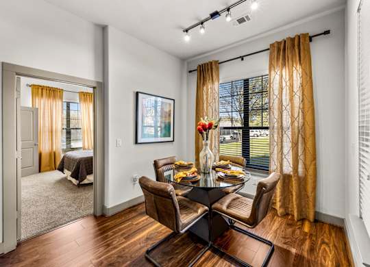 A dining room with a table set for two and a view of a bedroom through the door. at The Royce at 8100, Austin, TX