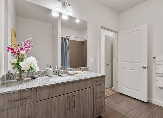 A bathroom with a vanity, mirror, and a vase of flowers.