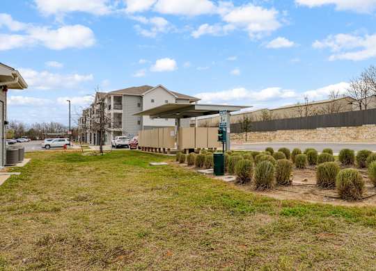 A grassy area with a building in the background and a parking lot with cars.