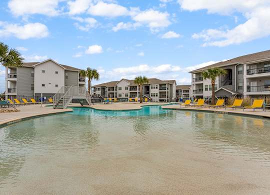 A swimming pool in front of apartment buildings with yellow lounge chairs.