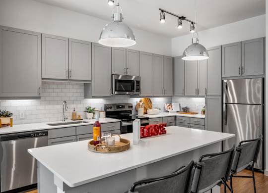 A modern kitchen with a white island and grey cabinets. at The Haywood Apartments, Texas
