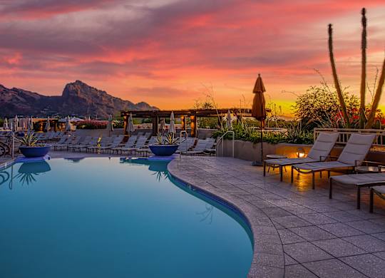 A poolside area with lounge chairs and a mountain in the background during sunset.