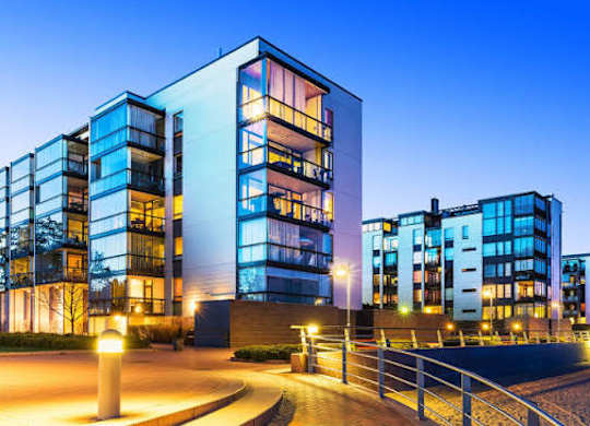 A modern building with glass windows and balconies is illuminated at dusk.