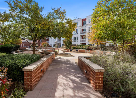 a walkway with benches and trees in front of an apartment building