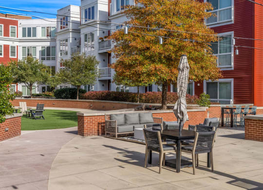 A patio with a table and chairs is surrounded by a brick wall and a tree.
