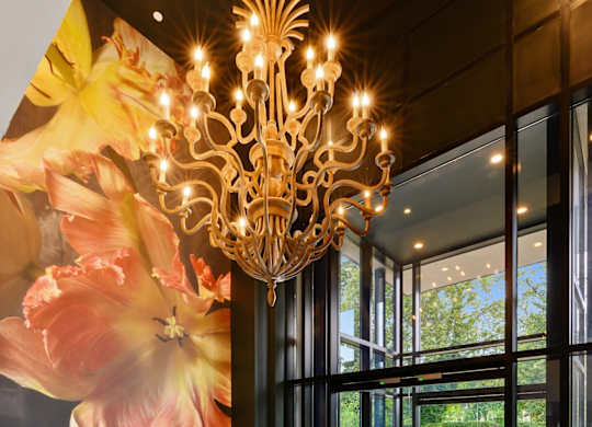 A large chandelier hangs over a grey rug in a room with a large mural of flowers on the wall.