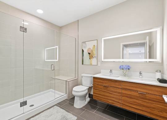 A modern bathroom with a glass shower stall, white toilet, and wooden vanity.