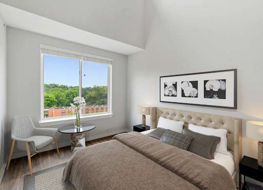 A bedroom with a large bed, a chair, a table, and a framed picture on the wall.