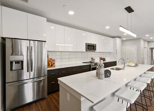 A modern kitchen with a long white counter and stainless steel appliances.