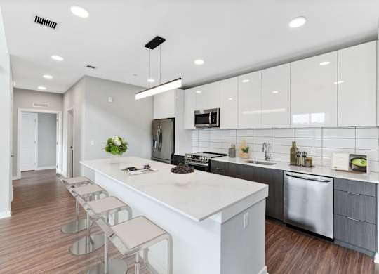 A modern kitchen with a long white island and stainless steel appliances.