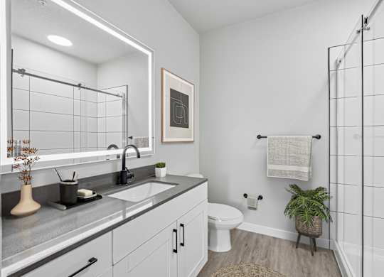 Model apartment bathroom with walk-in shower and backlit mirror