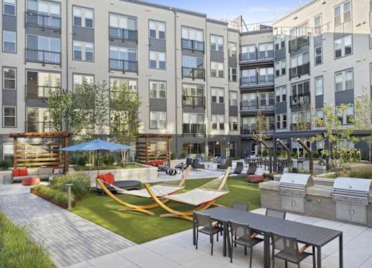 A modern outdoor seating area with tables and chairs is surrounded by apartment buildings.