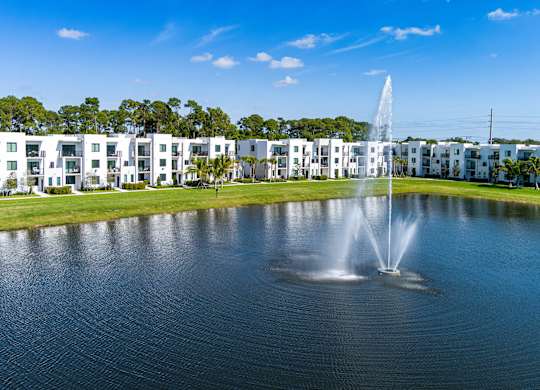 A fountain in the middle of a lake in front of apartment buildings.