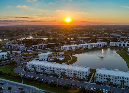 A sunset view of a residential area with a large white building and a fountain in the foreground.