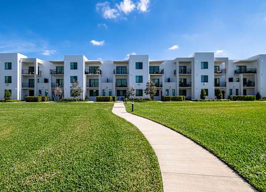 A row of white apartment buildings with a walkway in the foreground.