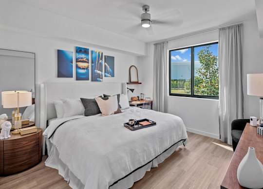 A bedroom with a large bed, a ceiling fan, and a view of the outdoors through a window.