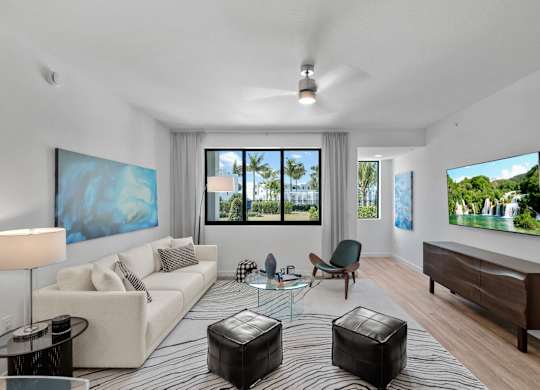 A modern living room with a large painting on the wall and a view of the outdoors through the windows.