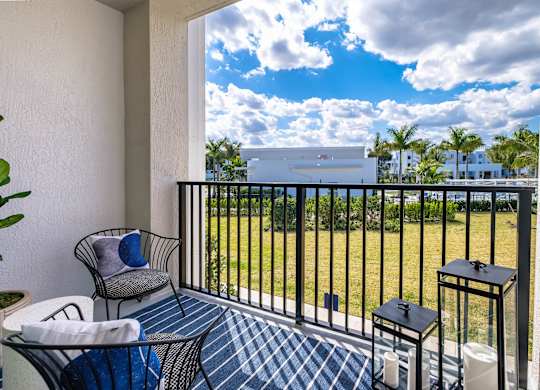 A balcony with a chair, table, and potted plant overlooking a grassy area.