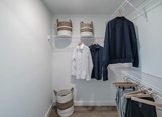 A white closet with clothes and baskets.