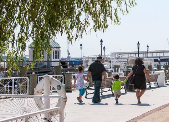 A family of three walks down a sidewalk past a no parking sign.