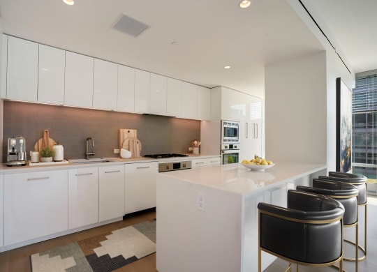 a kitchen with white cabinets and a white island with black chairs