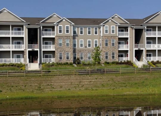 Building view of the property behind a lake style water feature and lots of natural grass at Chesapeake Ridge, Maryland, 21901