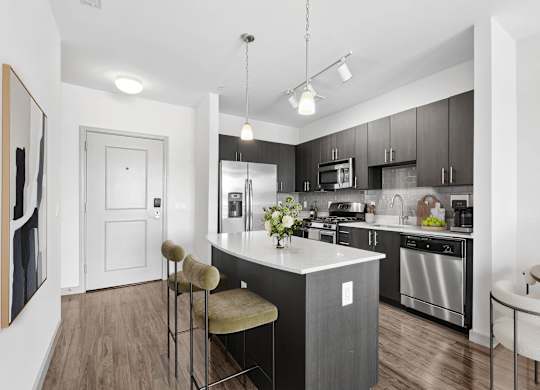 Kitchen at 7001 Arlington at Bethesda in Bethesda, MD, featuring quartz countertops, espresso cabinetry, a center island with seating, tile backsplash, and stainless-steel appliances.