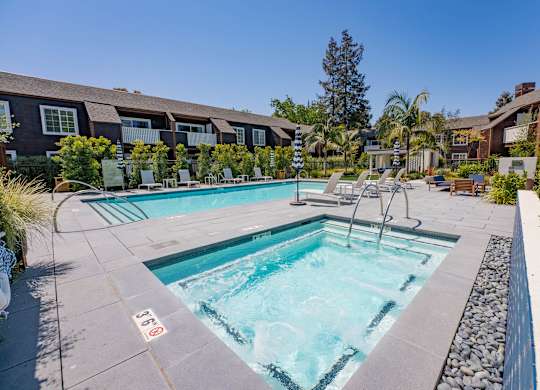 A swimming pool surrounded by a stone border and lounge chairs.