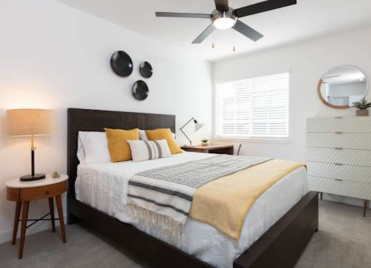 A bedroom with a bed, a ceiling fan, and a nightstand with a lamp.