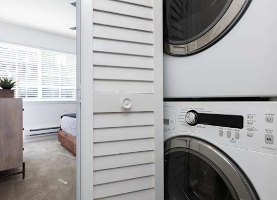 A washing machine is in the foreground of a laundry room.