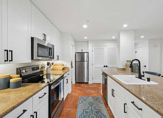 Modern apartment kitchen at Marlin Cove Apartments with white cabinetry, granite countertops, and stainless steel appliances.