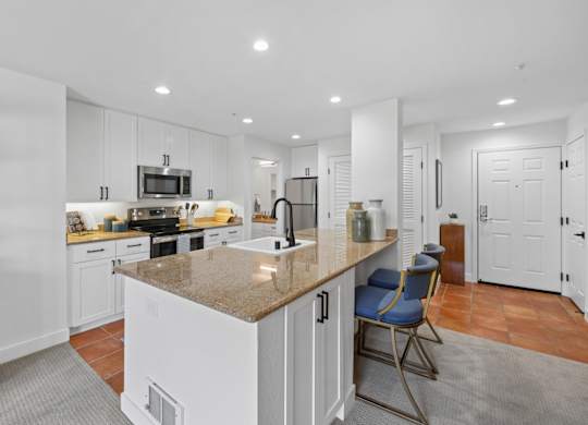 Modern kitchen at Marlin Cove Apartments with granite island, white cabinetry, and stainless steel appliances.