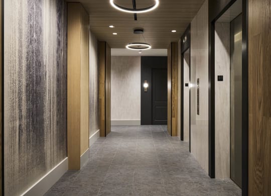 a long hallway with wood paneled walls and a gray floor and a black door