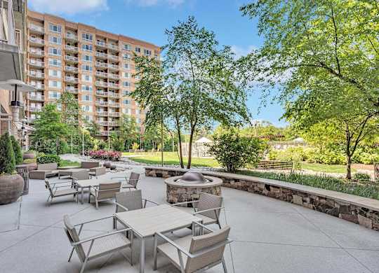 A patio with tables and chairs is surrounded by trees and a stone wall.